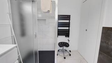 Un baño con cabina de ducha de vidrio, un perchero, una silla negra y suelo de baldosas.
