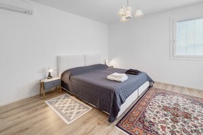 Un dormitorio con cama, mesita de noche, lámpara y dos alfombras.