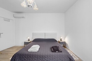 A bedroom with a bed, bedside lamps, a nightstand, a wall-mounted air conditioner, and a ceiling light fixture. - Twin Room with Air Conditioning (San Donà di Piave)