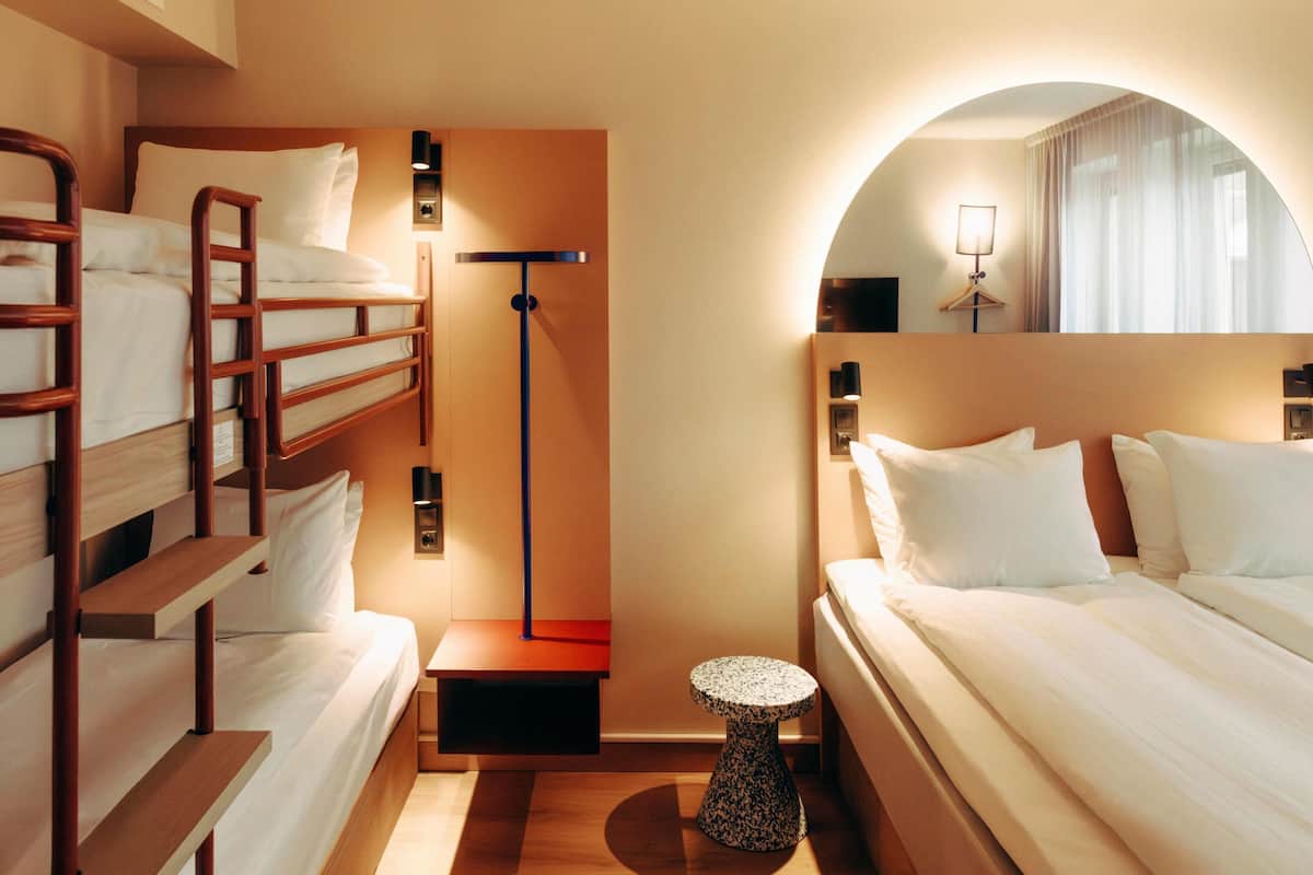 A hotel room with a bunk bed, a small round table, a lamp, and a mirror.