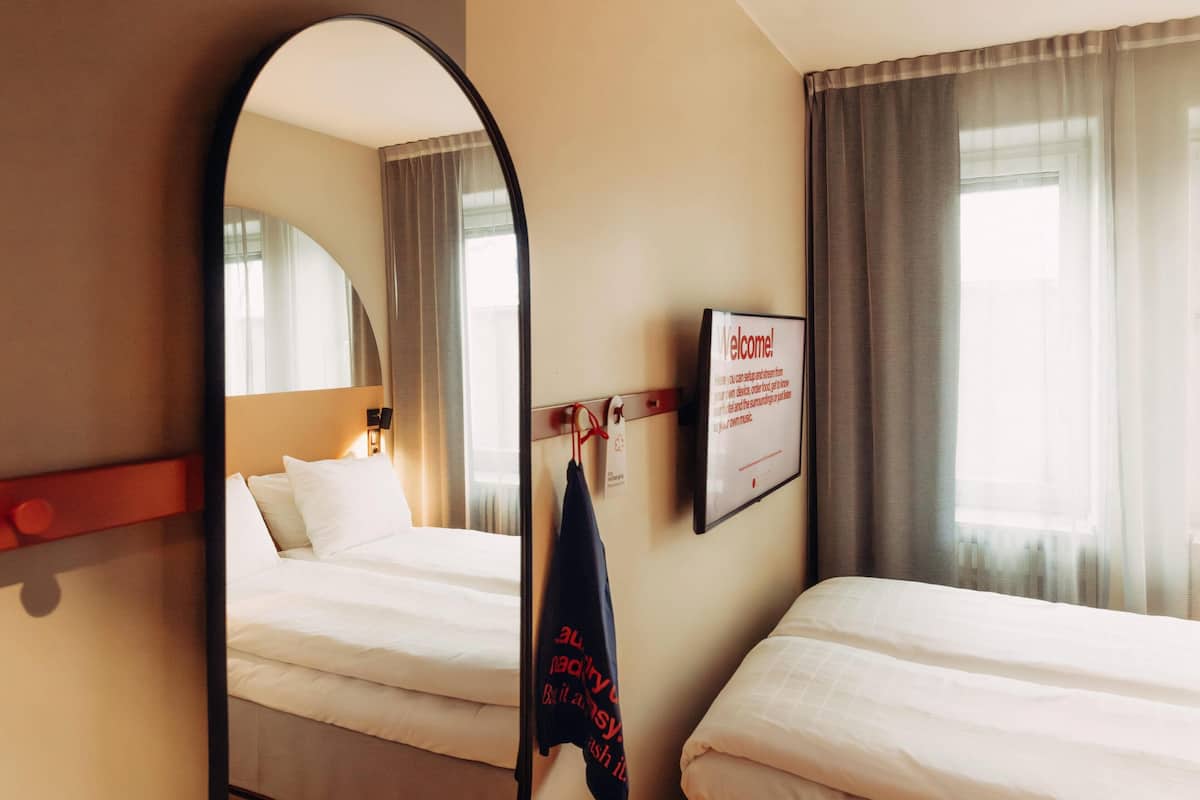 A hotel room with two beds, a large mirror, a welcome sign, and a coat hanging on the wall.