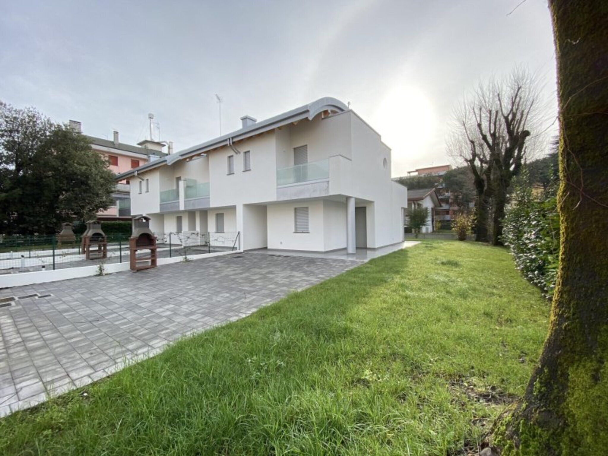 Un edificio moderno con techo plano, patio empedrado y zona ajardinada.