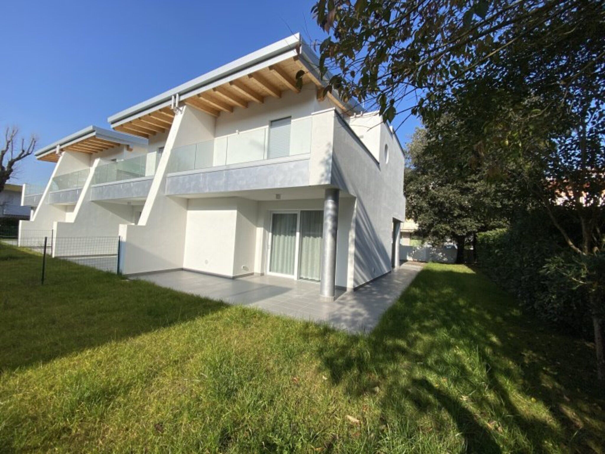 A modern two-story house with a flat roof, large windows, and a covered patio area.