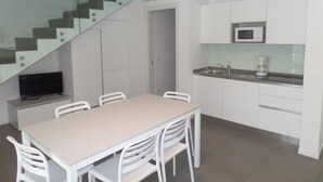 A modern kitchen with white cabinets, a microwave, and a coffee maker. There is a dining table with chairs and a television on a stand. A glass staircase is visible in the background. - Bright Family Villa With Garden Close to the sea (San Michele al Tagliamento)