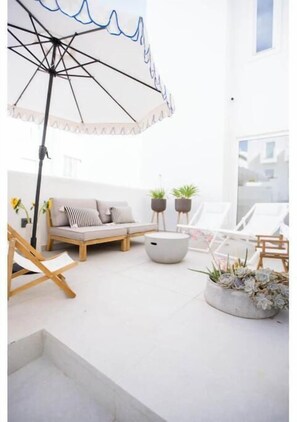 Ein moderner Außenbereich mit Sitzgelegenheiten, einer Couch, Lounge-Stühlen, einem Sonnenschirm und Topfpflanzen.