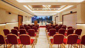 A conference room with rows of red chairs, a podium, and a large screen. -  Hotel Grand Royal Paika (POOVARANI)