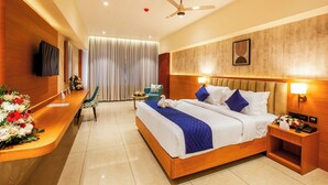 A hotel room with a bed, bedside table, TV, and a desk with chairs. -  Hotel Grand Royal Paika (POOVARANI)