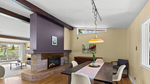 A modern dining room with a fireplace, wooden flooring, and a large window. - West End 4BR  Stay Patio BBQ Firepit  WiFi Parking (St. John's)