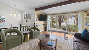 A modern living room with a sofa, chairs, a round table, a bench, a TV, and large windows with a view. - West End 4BR  Stay Patio BBQ Firepit  WiFi Parking (St. John's)