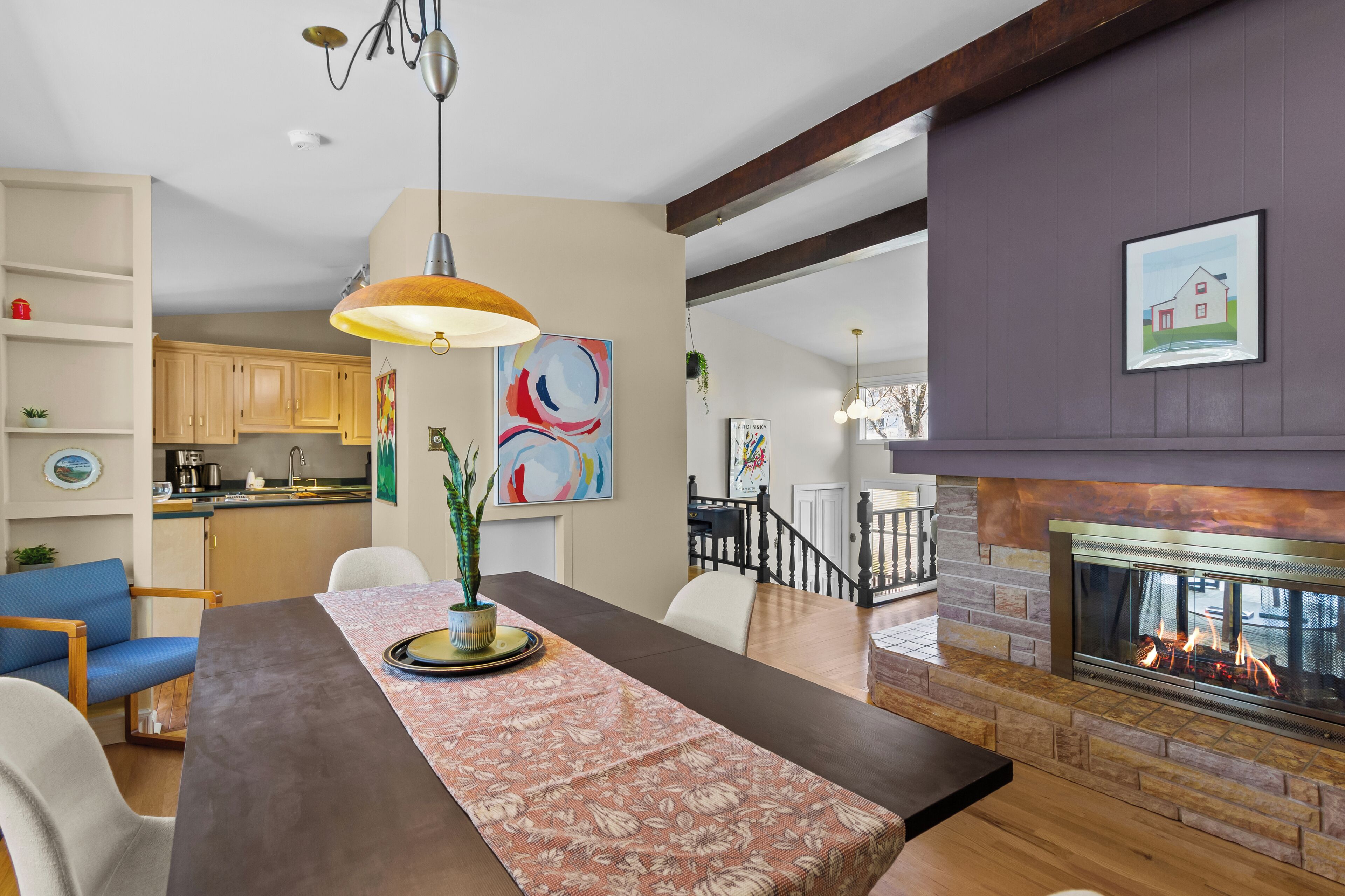 A dining area with a long table, chairs, a hanging pendant light, and a fireplace.
