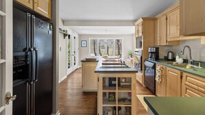 A kitchen with wooden cabinets, a black refrigerator, a central island, and a view of trees through large windows. - West End 4BR  Stay Patio BBQ Firepit  WiFi Parking (St. John's)