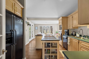 A kitchen with wooden cabinets, a black refrigerator, a central island, and a view of trees through large windows.