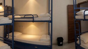 A bunk bed room with a wooden door, a black trash bin, and a wall-mounted light. - Kattil (Madurai)