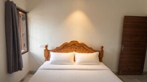A neatly made bed with a wooden headboard, a window with curtains, and a door. - Kattil (Madurai)