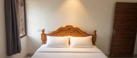 Una cama bien tendida con un cabecero de madera, una ventana con cortinas, y una puerta.