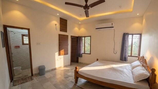 A bedroom with a wooden bed, an air conditioning unit, and a ceiling fan. - Kattil (Madurai)