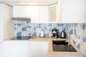 A modern kitchen with white cabinets, a stainless steel coffee maker, and a black sink.
