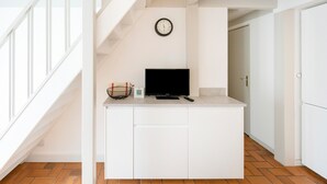 Een moderne keuken met een ingebouwde televisie, een klok aan de muur, en een trap naar een andere kamer.