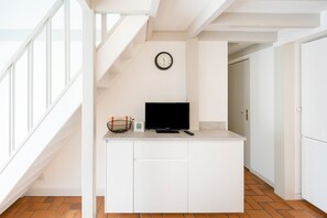 A modern kitchen with a built-in TV, a clock on the wall, and a staircase leading to another room.