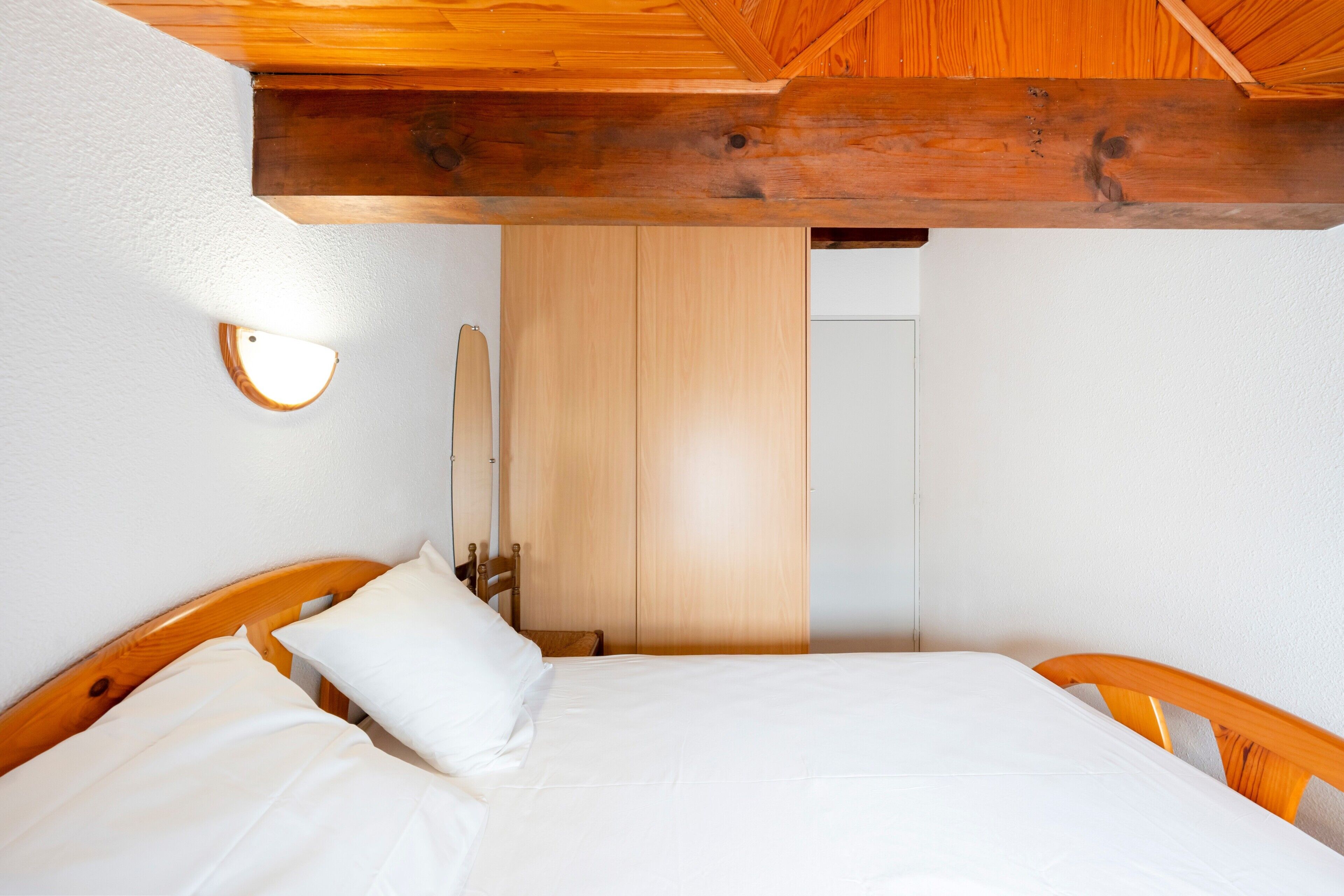 Un dormitorio con estructura de cama de madera, ropa de cama blanca, techo de madera y un armario de madera.