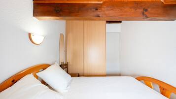 Un dormitorio con estructura de cama de madera, ropa de cama blanca, techo de madera y un armario de madera.