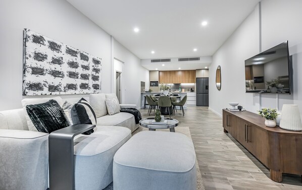 Un salon moderne comprenant un canapé, un pouf et un coin repas avec des chaises et une table.