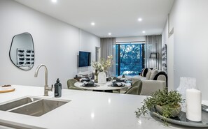 A modern kitchen with a sink, a dining area with a table set for four, and a living area with a sofa and a TV. - Luxury Burswood Stay · Crown, Stadium & Swan River · Sleeps 6 (Burswood)