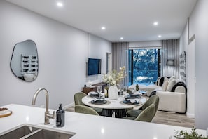A modern dining area with a round table, chairs, and a kitchen counter with a sink. - The Signature: 3BR, Crown & Stadium, Rooftop BBQ (Burswood)
