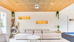 Uma sala de estar moderna com um sofá, mesa de bilhar e teto de ripas de madeira.