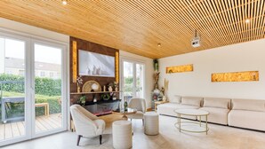 Uma sala de estar moderna com teto de madeira, janelas amplas, um sofá, uma mesa de centro e uma lareira.