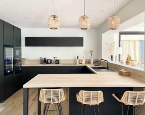 Eine moderne Küche mit schwarzen Schränken, einer Holz Arbeitsplatte, einer großen Kochinsel mit Barhocker und drei Weidenkorb-Pendelleuchten.