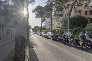 Una strada fiancheggiata da auto e motociclette parcheggiate, alberi e edifici a più piani.