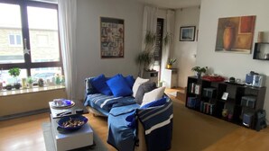 Ein Wohnzimmer mit einer Couch, einem Couchtisch, einem Bücherregal und einem Fenster mit Vorhängen.