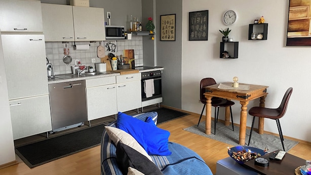 Eine moderne Küche mit weißen Schränken, einer Mikrowelle und einem Essbereich mit einem Holztisch und Stühlen.