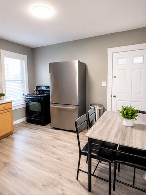 A modern kitchen with a stainless steel refrigerator, a stove, and a dining table with chairs. - 2-bedroom apartment in Lewiston near CMCC (Lewiston)