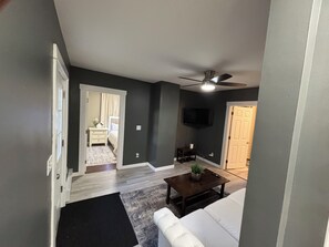 A living room with a ceiling fan, a television mounted on the wall, and a door leading to another room. - 2-bedroom apartment in Lewiston near CMCC (Lewiston)