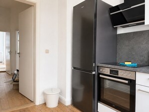 Eine moderne Küche mit einem Edelstahl-Kühlschrank, Backofen und einer Mikrowelle, einer weißen Mülltonne und einer grauen Arbeitsplatte.