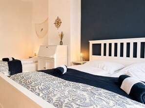 Ein Schlafzimmer mit Bett, Nachttischen, einer Kommode, einem an der Wand befestigten Kompass und einer Vase mit getrockneten Blumen.