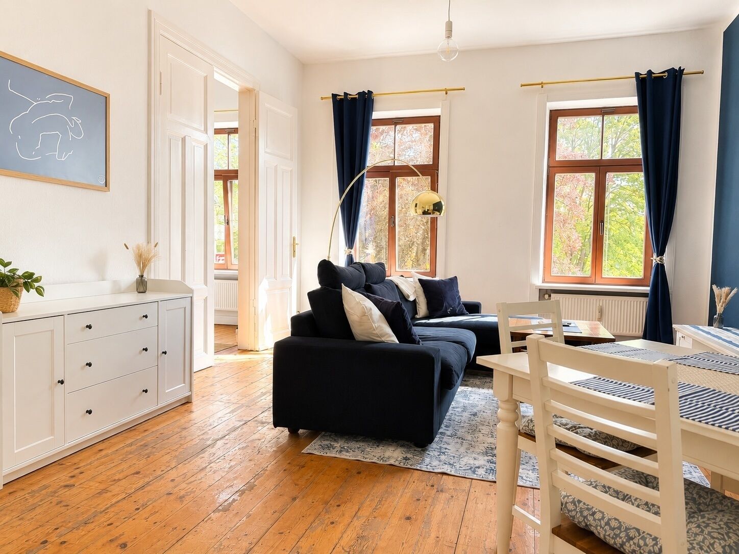 A room with a sofa, a desk, a chair, a lamp, and a window with curtains.