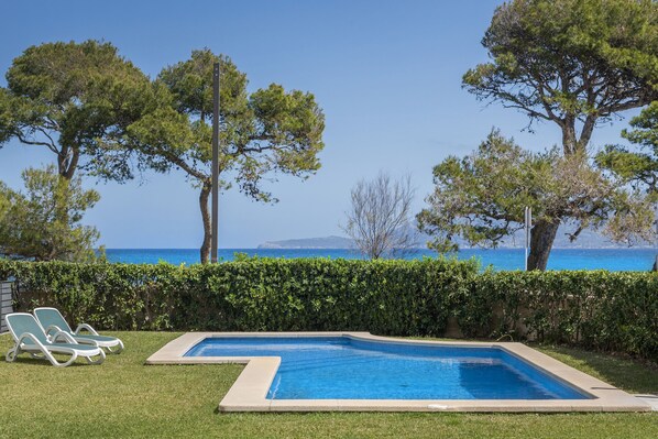 Ein Schwimmbecken mit Liegestühlen, umgeben von Hecken und Bäumen, mit Blick auf das Meer.