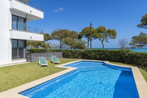 Ein modernes, zweistöckiges Gebäude mit Swimmingpool, zwei Liegestühlen und Meerblick.