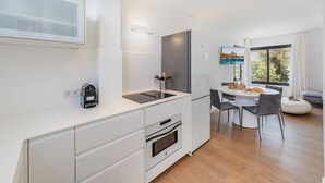 A modern kitchen with a built-in oven, a coffee machine, and a dining area with a round table and chairs. - APARTAMENTO ORATGE 2 (Puerto Pollensa)