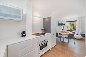 A modern kitchen with a built-in oven, a coffee machine, and a dining area with a round table and chairs. - APARTAMENTO ORATGE 2 (Puerto Pollensa)
