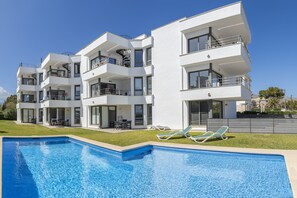 Ein modernes Mehrfamilienhaus mit Balkonen, einem Swimmingpool und Liegestühlen.