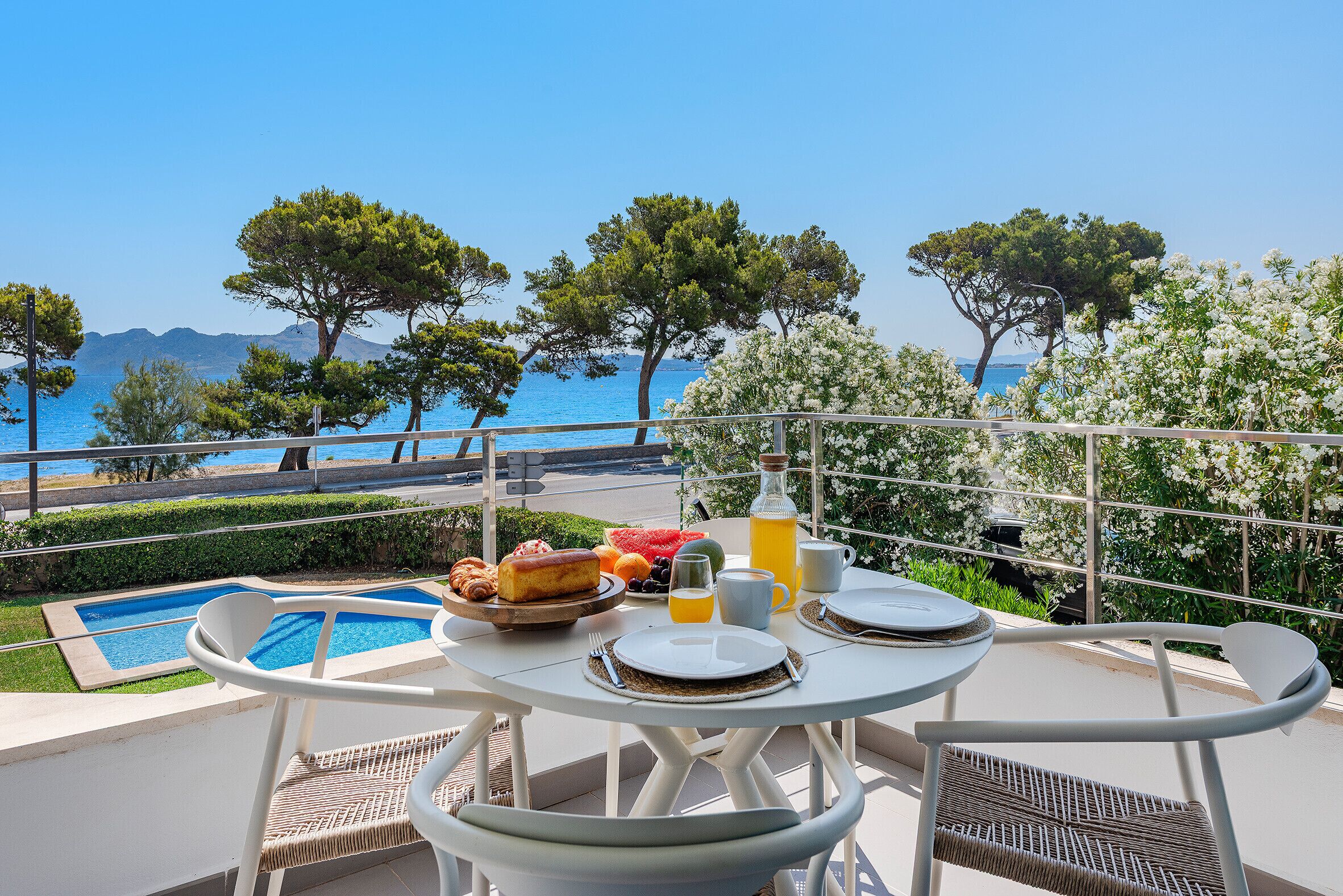 A balcony with a pool, dining table, chairs, and a view of the sea.