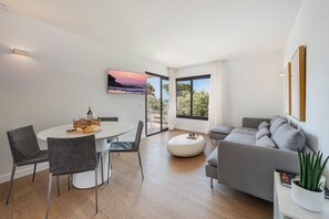A modern living room with a dining area, a grey sofa, a round coffee table, and a large window with a view. - APARTAMENTO ORATGE 2 (Puerto Pollensa)