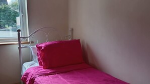 A single bed with a metal frame, a window with a view of trees, and a wooden floor.