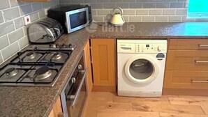 A compact kitchen with wooden cabinets, a microwave, a stove, and a washing machine.