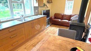 A kitchen with wooden cabinets, a dining table, a sofa, and a wood-burning stove.