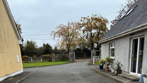 A gravel driveway leading to a house with a stone wall and a metal gate.